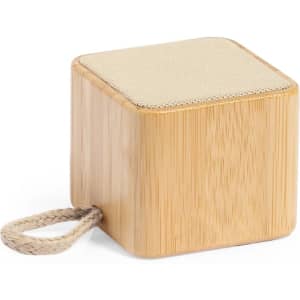A compact wooden speaker in a natural bamboo finish with a fabric top and a braided handle.