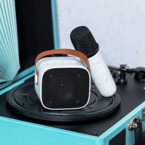 A white karaoke speaker with a brown handle and a microphone, resting on a turntable with a blue casing.
