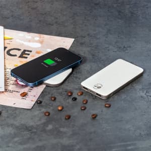 A wireless charger in black and white sits on a textured surface, alongside scattered coffee beans and a menu.