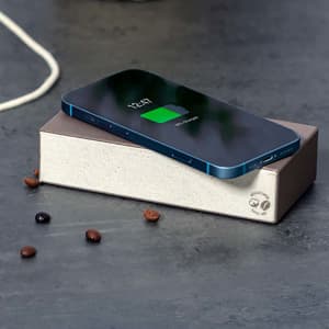 A wireless charger in a stone-coloured design with a phone displaying a charging status on its surface.