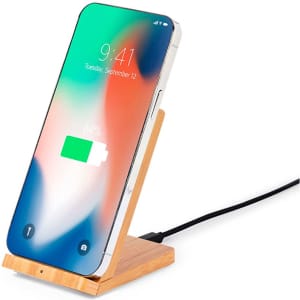 A wireless charger with a wooden stand displays a smartphone charging, featuring a green battery icon and vibrant screen.