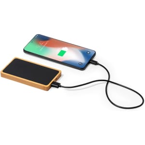 A power bank in a bamboo design connected to a smartphone, displaying a charging indicator.