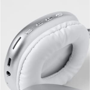 A pair of silver headphones with white padding, featuring control buttons and a charging port.