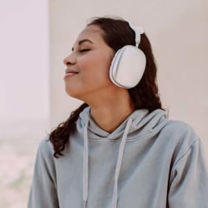 A pair of white headphones worn by a person with curly hair, enjoying music while wearing a grey hoodie.