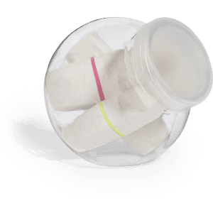 A jar containing highlighter sticks in pink, yellow, and white, with a clear lid and a logo visible on the jar.