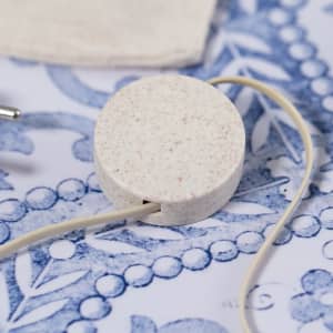 A round, speckled charging pad in off-white, with a connected charging cable, sits on a decorative blue surface.