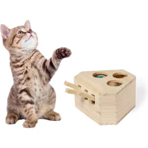 A tan and brown striped cat reaches out next to a wooden toy with holes and levers, resembling cheese.