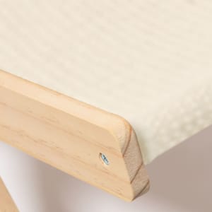 A wooden edge of a pet chair featuring a light cream cushion. The chair has a simple design and natural finish.