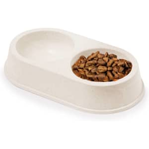 A beige pet bowl with two compartments, one filled with dry pet food and one empty. It features a logo.