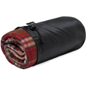 A rolled-up blanket in red plaid and brown, secured with a black fabric strap, featuring a small logo.