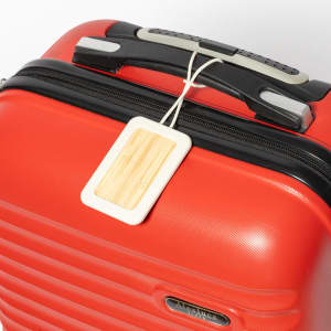 A red luggage suitcase featuring a beige luggage tag with a wooden texture attached to the handle.