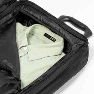 A black wheeled bag containing a folded light green shirt inside. The bag features a handle for easy transport.