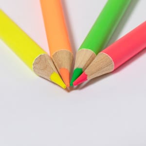 A set of four wooden pencils in yellow, orange, green, and pink arranged together at the tips.