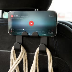 A black car phone holder attaches to a headrest, holding a smartphone displaying a video.