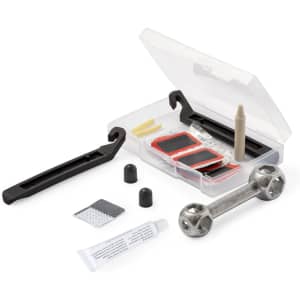 A bike repair kit in a clear case, including tyre levers, patches, a glue tube, and a metal tool, featuring black and silver colours.
