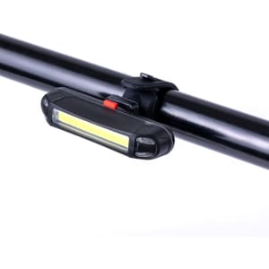 A black bike safety light attached to a bike handlebar, featuring a white LED strip and a red on/off switch.