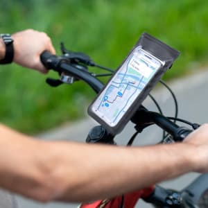 A mobile phone secured in a transparent holder on a bicycle handlebar, featuring a map display and greenery in the background.