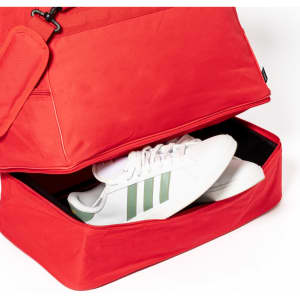 A red duffle bag with a compartment containing white sneakers with green stripes and a clip-on pouch.