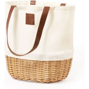 A cream canvas picnic basket with a woven wicker base and brown leather handles. It features a simple design and has a logo.
