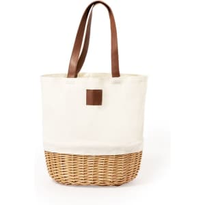 A cream and woven wicker picnic basket with brown leather handles and a simple logo patch.