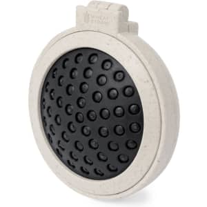 A circular hairbrush in beige with a black bristle pad, featuring a textured design. Includes a branding logo.