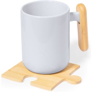 A grey mug with a wooden handle sits on a bamboo coaster shaped like a puzzle piece. The coaster has a logo.