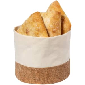A bread basket featuring a cream fabric body and a cork base, holding several golden-brown bread pieces.