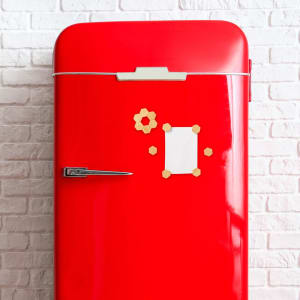 A vibrant red fridge adorned with decorative magnets in beige shapes, including a square and a gear design.