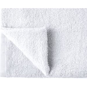 A soft white bath towel with a textured surface and folded corner. It features a small branding logo.
