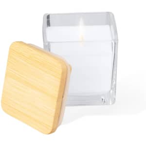 A square, clear glass candle with a white wax interior and a bamboo lid, featuring a lit wick.