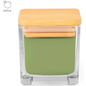A green aromatic candle in a clear glass container with a wooden lid. It features a logo on the top.