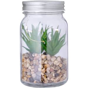 A decorative plant in a clear glass jar, featuring green artificial foliage and a base of small pebbles.