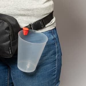 A clear plastic cup holder with a red clip attached to a person’s waistband, alongside a black bag.