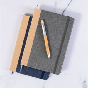 A wooden pen rests atop two notebooks in grey and navy blue, featuring a textured cover and elastic closure.