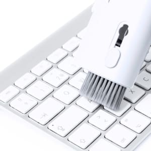 A cleaning brush in white being used on a silver keyboard, featuring a logo on the brush handle.