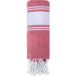 A red and white striped hand towel pareo with tassels at the ends and a simple design. It features a logo.