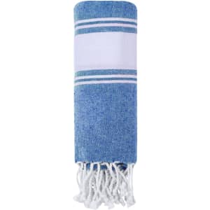 A blue and white striped towel, elegantly styled with fringe detailing at the ends and a branding logo.