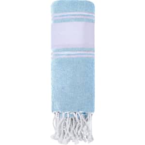 A light blue towel pareo with white and pink stripes and fringe detailing, featuring a brand logo.