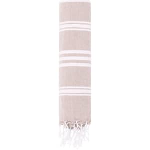 A Harlow Towel Pareo in a light brown colour with white stripes and fringed edges. It includes a branding logo.
