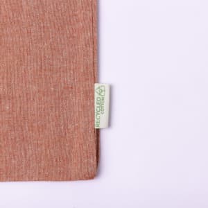 A peach-toned tote bag made from recycled materials with a small label indicating its eco-friendly composition.