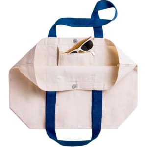 A cream tote bag with navy handles, featuring an inner pocket containing sunglasses. It has a logo.