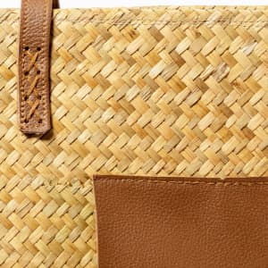 A textured straw tote bag with brown leather accents and a front pocket.