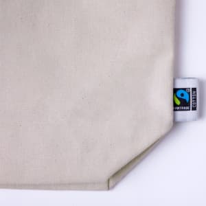 A cream-coloured tote bag with a textured fabric and a small Fairtrade logo tag.