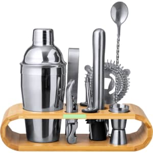 A cocktail set featuring a silver shaker, strainer, stirrer, and jigger, presented on a bamboo storage stand.