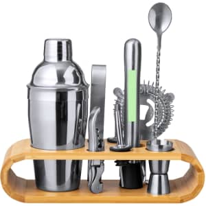 A stainless steel cocktail shaker set with a bamboo stand, including various tools like a strainer, jigger, and stirrer.
