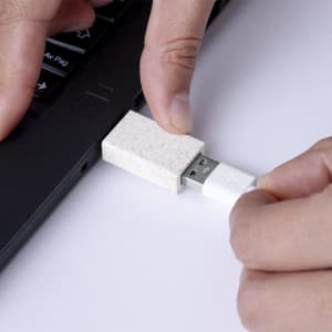 A USB drive with a textured white casing is being plugged into a laptop's USB port.