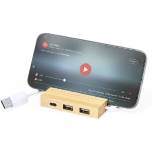 A bamboo USB hub with multiple ports, positioned in front of a smartphone displaying a video.