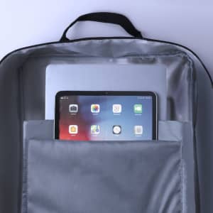 A grey backpack interior features a laptop and a tablet in designated pockets. The backpack includes a logo.