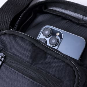 A black shoulder bag with a zipped pocket containing a smartphone. The interior shows a grey lining.