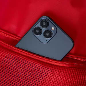 A smartphone is partially visible in a red drawstring bag with mesh detailing. The bag features a logo.